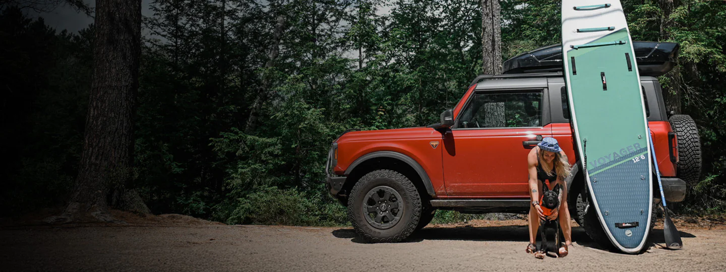 Woman and dog by orange Ford Bronco® SUV and paddleboard